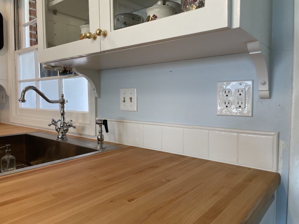 Electrician moved double duplex electrical outlet leftward to accomodate new wood cabinet corbels. Installed jolly tiles above new 4 inch bacsplash tiles.
