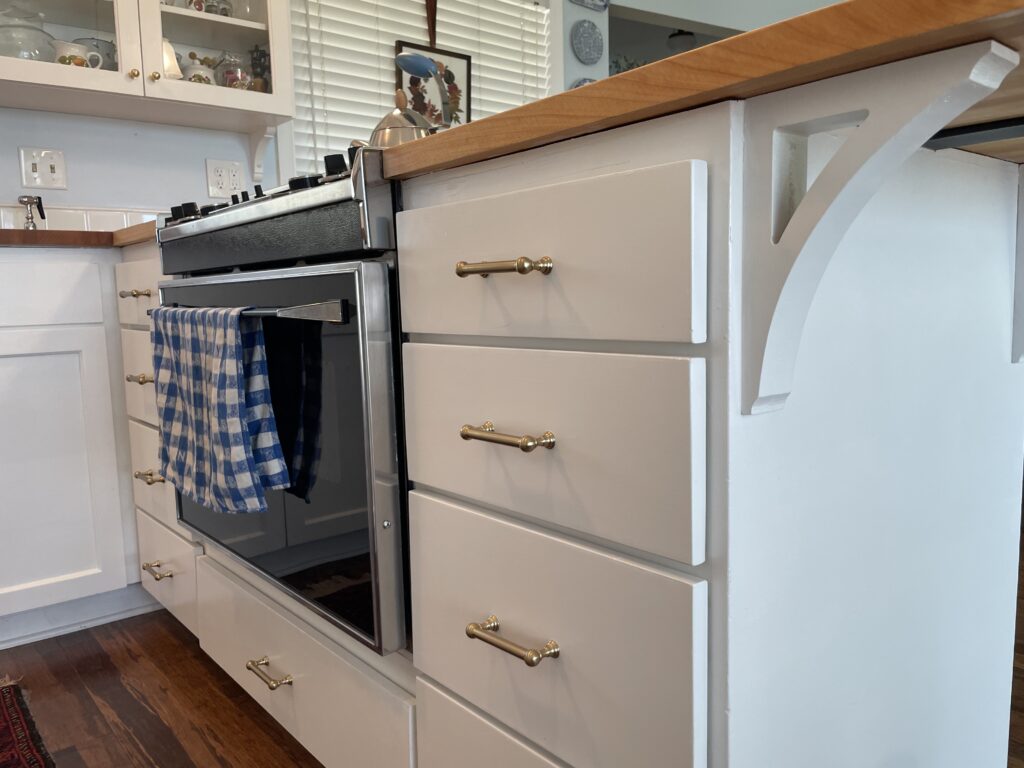New drawer pulls and cabinet knobs after repainting all exposed cabinet and drawer services white. New white painted decorative corbel.