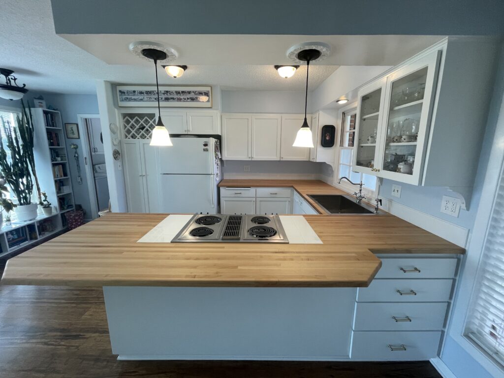 Kitchen remodel by Action Craftworks LLC in Vancouver WA, site view, completed after painting cabinets and installing Maple wood sustainable butcher block countertops, finished with Rubio Monocoat Oil Plus 2C Pure, can lights replaced with pendant lamps, and new sink and faucet set.